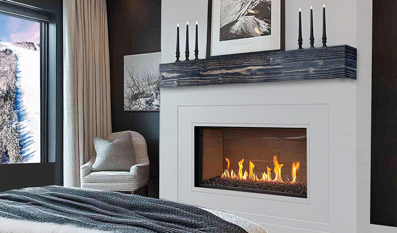 Modern bedroom with a fireplace, cozy chair, large window showing snowy trees, and neutral decor.