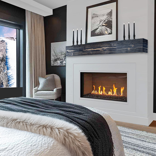 Modern bedroom with a fireplace, cozy chair, large window showing snowy trees, and neutral decor.