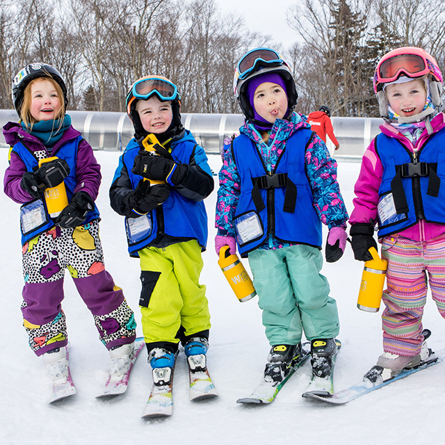 Group of children in colorful ski outfits smiling on a snowy slope.